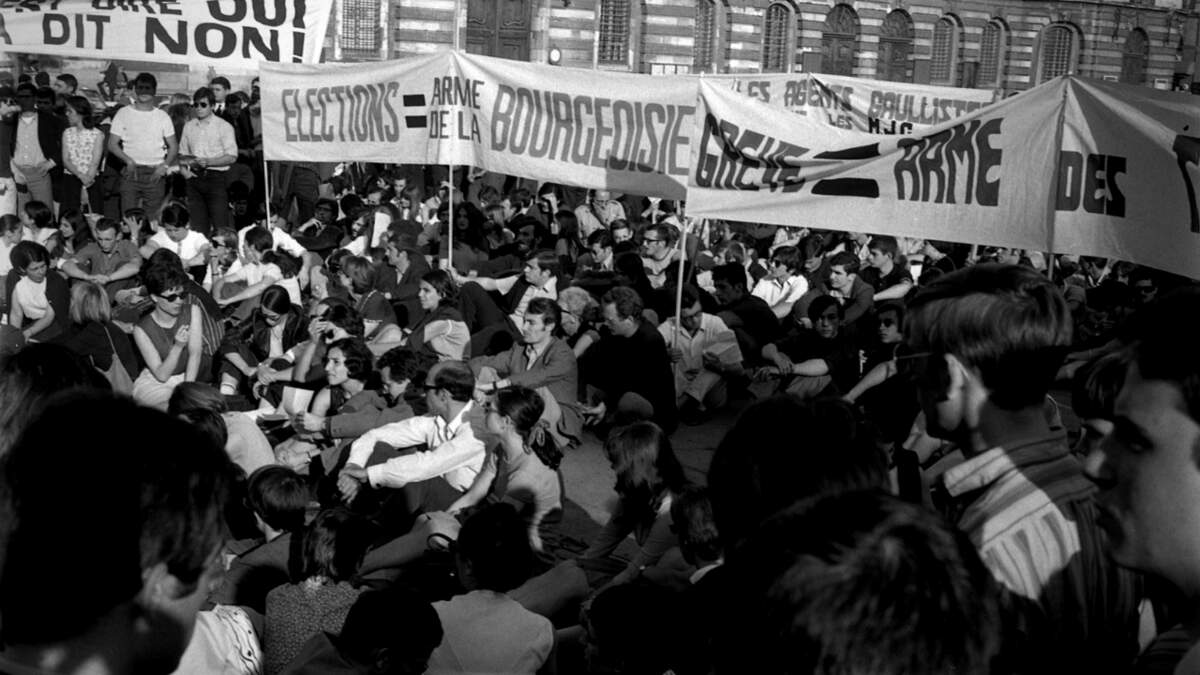  Place du Capitole. 11 ou 12 juin 1968. Vue d’ensemble en contre-plongée des manifestants, une partie d’entre-eux sont assis par terre. Cliché pris durant les évènements de Mai 68 à Toulouse.