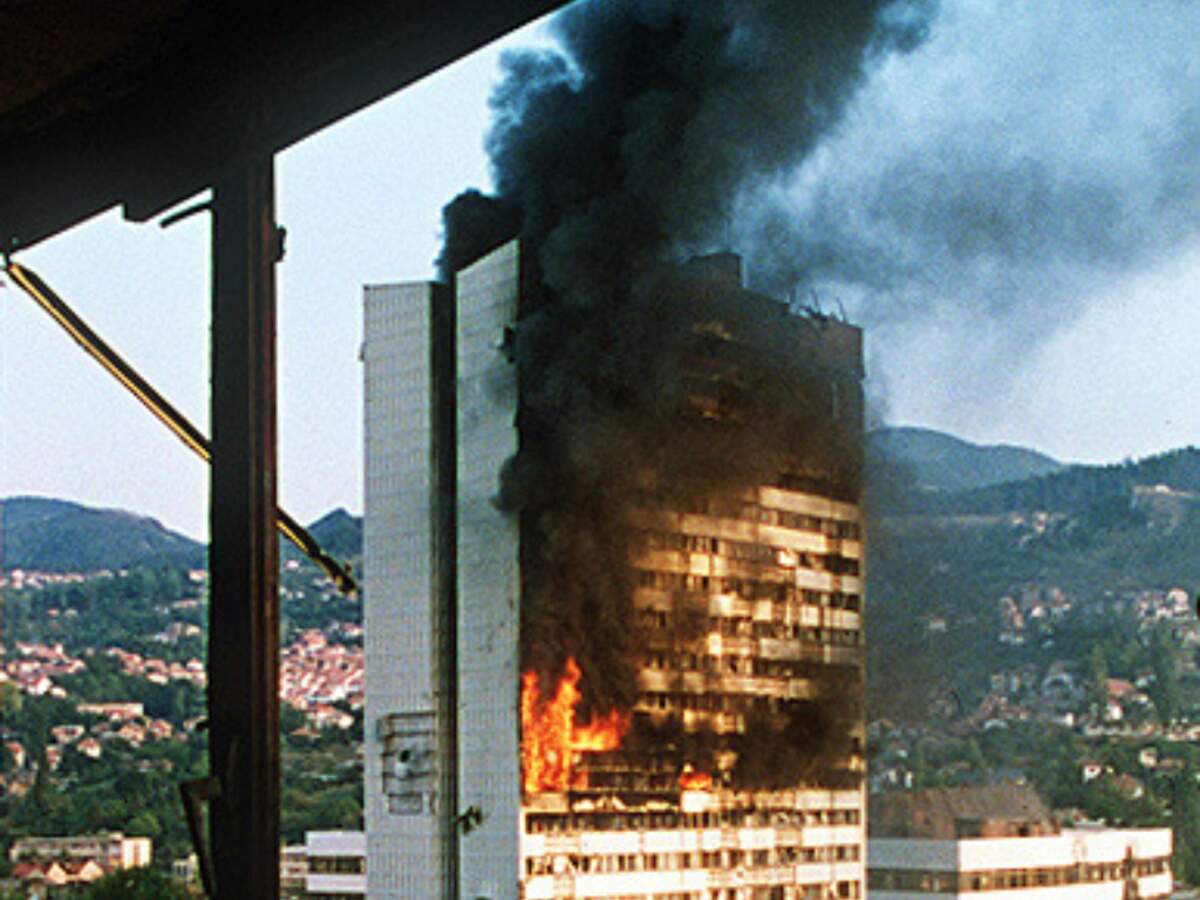 Le bâtiment du parlement de Sarajevo en flammes après avoir reçu un obus de char, en 1992 · Via Wikimédia